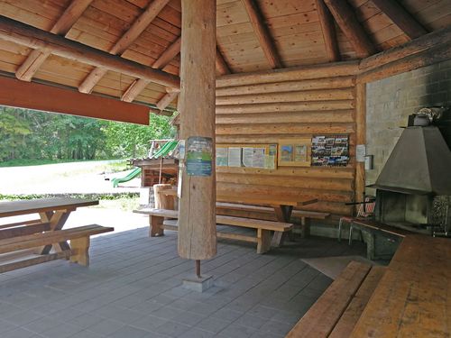 Gedeckte Rundholzhütte mit Feuerstelle, Tischen und Bänken